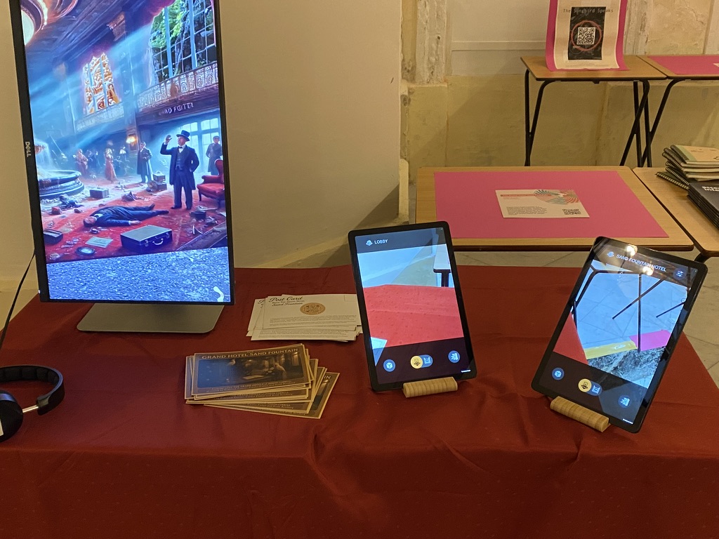 The Grand Hotel Sand Fountain installation table with a monitor, two tablets, postcards, and headphones at ICIDS 2025.